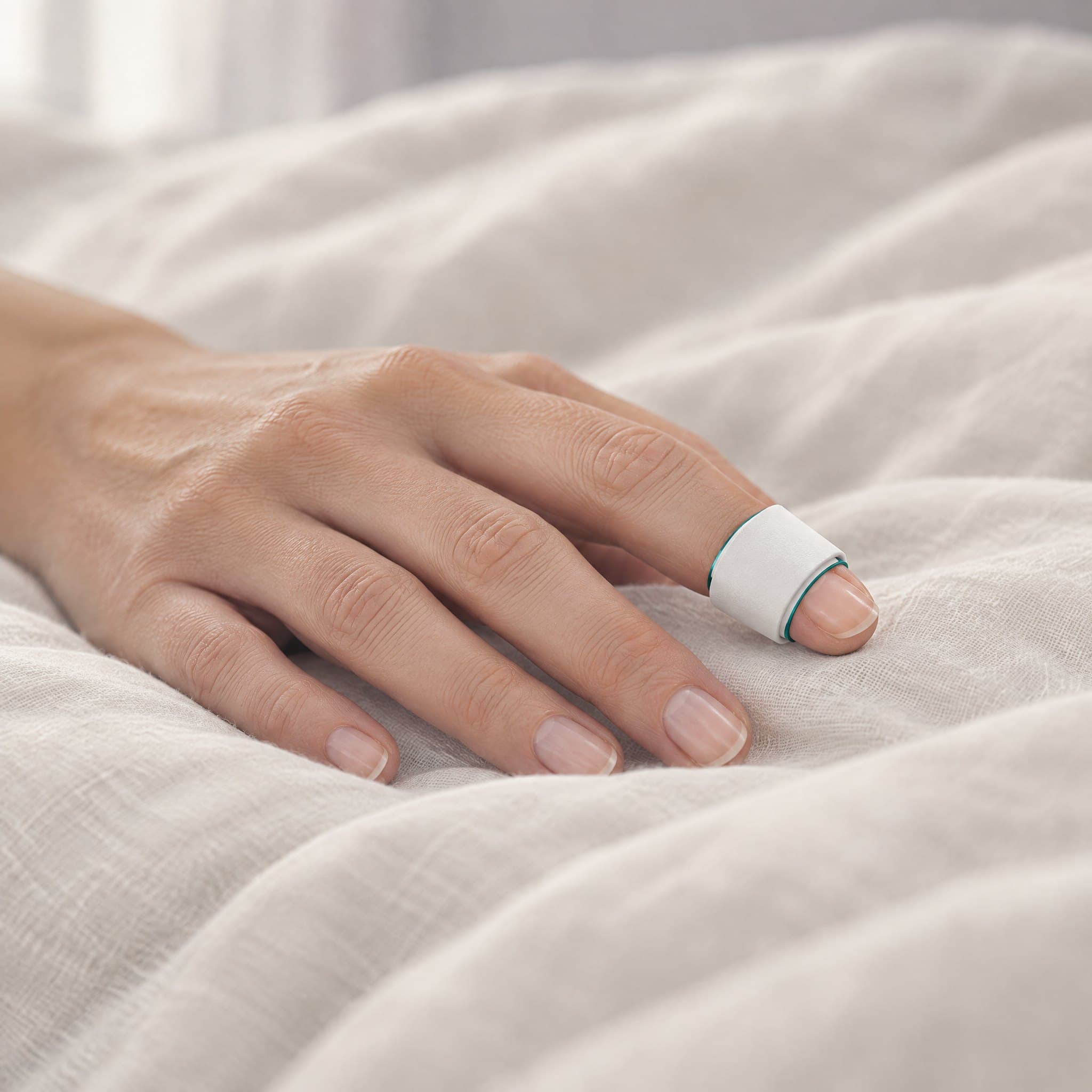 A hand resting on bedding with the sensor held on the index fingertip by a white wrap